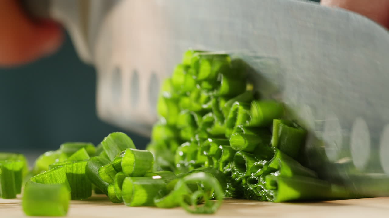 Cutting fresh green onions on a cutting board, close up chef cooking green vegan salad.