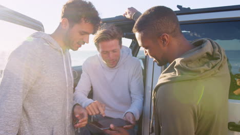 Three-young-men-using-tablet-computer-by-their-car