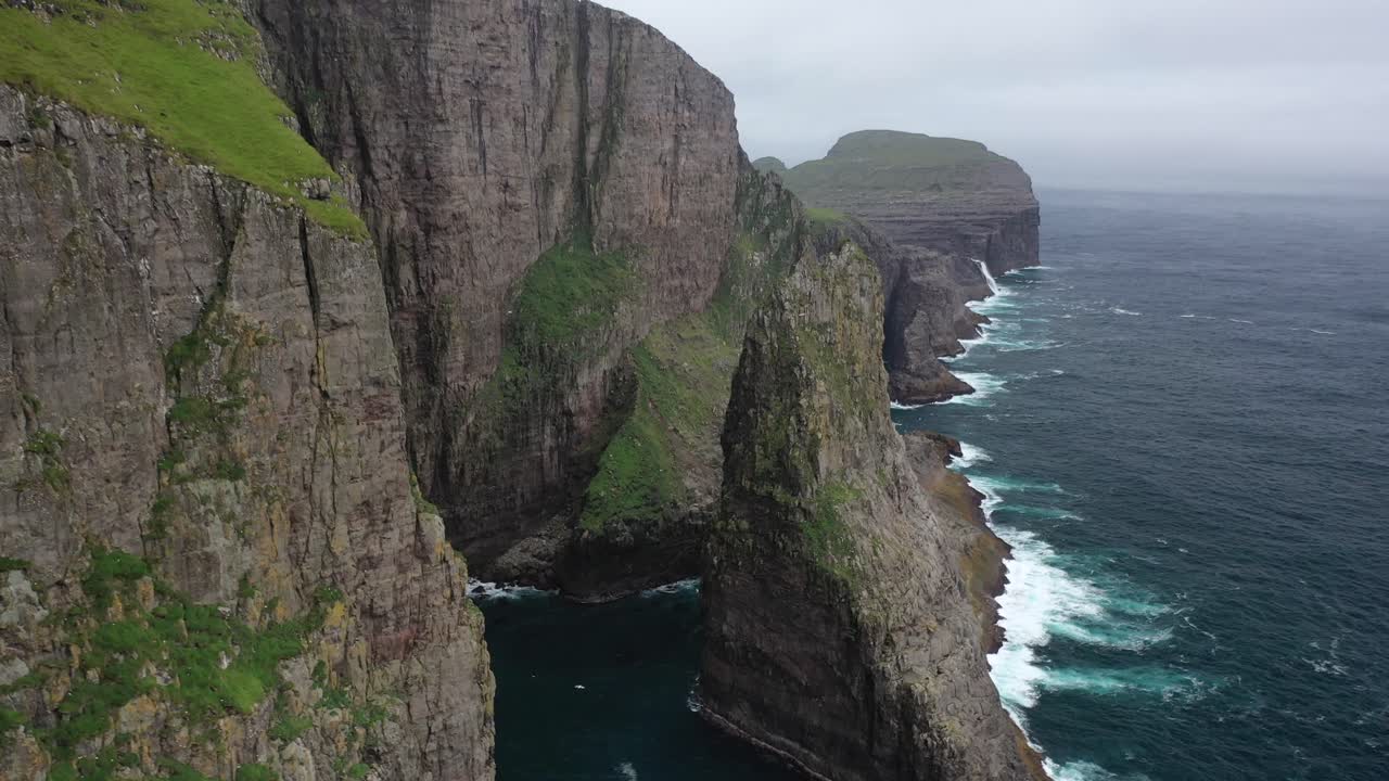Flight through cliffs with seabirds flying along Faroe Islands coastline, drone