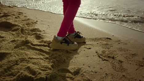 little girl legs walking on sea beach sand. child feet going away crashing waves