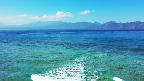 An-Island-In-Tonga-Tropical-Paradise-Bright-Blue-Sea-Water-With-Beautiful-Mountain-In-The-Background-waves-rolling-on-the-coral-reef