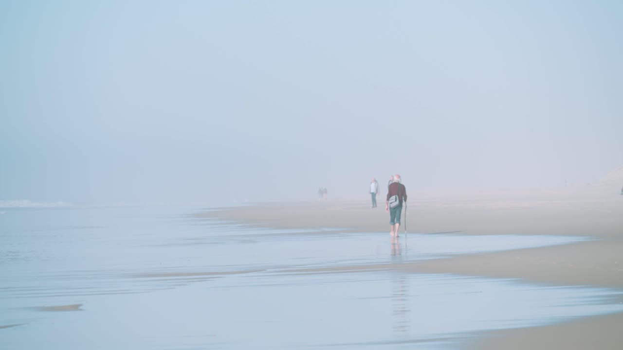 A peaceful misty morning on a sandy beach with people walking. slow motion