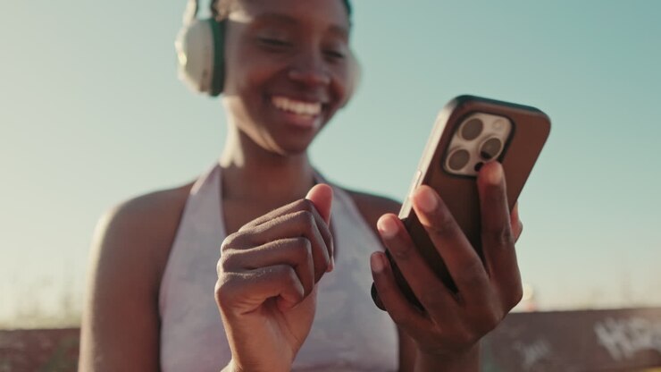 Giovane donna afroamericana sorridente che usa lo smartphone con le cuffie