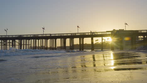 dolly shot moving backwards along the the ventura beach while waves crash along the shore with the ventura pier and sunsetting in the background located in southern california