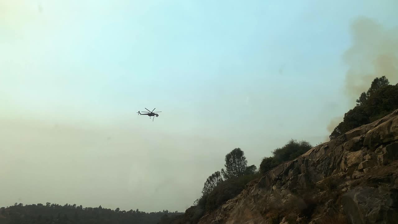 toma de conducción pov de un helicóptero arrojando agua sobre un incendio forestal en las tierras altas