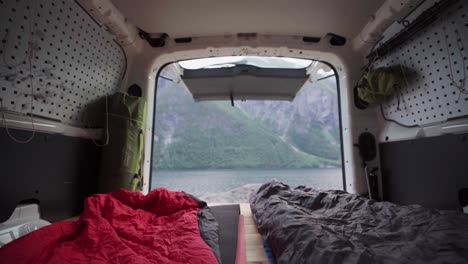 view of fjord and rocky mountain from bed inside a camper van in norway