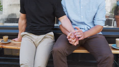 close up of loving male gay couple holding hands outside coffee shop