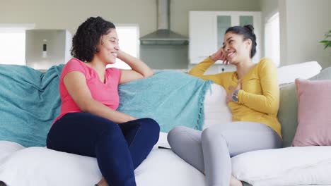 Two-diverse-female-friends-talking-and-laughing-sitting-on-couch-at-home,-in-slow-motion