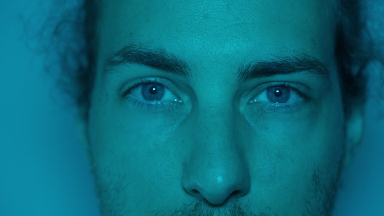 Portrait of a man with wide eyes, blue-tinted lighting adds an intense, curious atmosphere, macro shallow depth of field