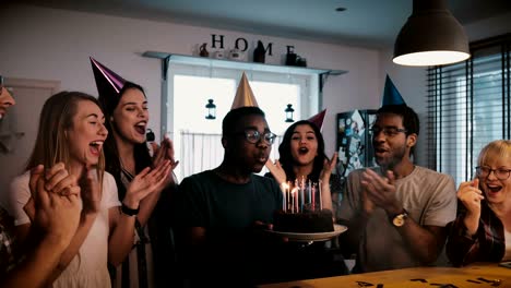 happy african american young man holding birthday cake with candles, celebrating with multiethnic friends slow motion 4k