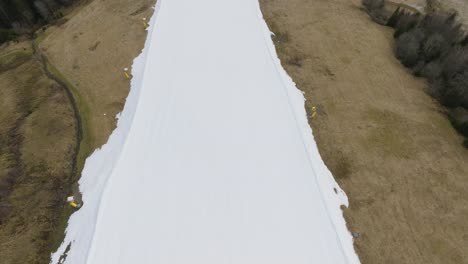 A-snowy-ski-slope-in-Saalbach-Hinterglemm-without-skiers,-bordered-by-dry-grass,-aerial-view