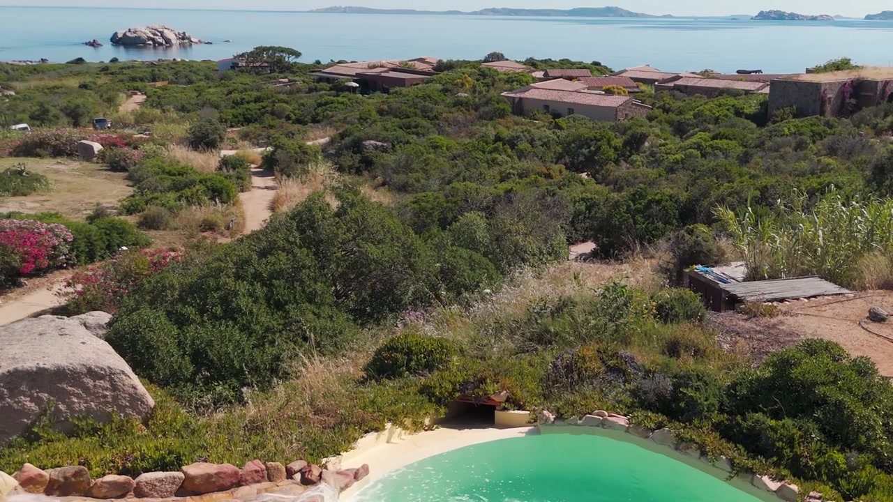 Vista aérea de vilas cercadas por vegetação mediterrânea perto de uma piscina turquesa e do mar