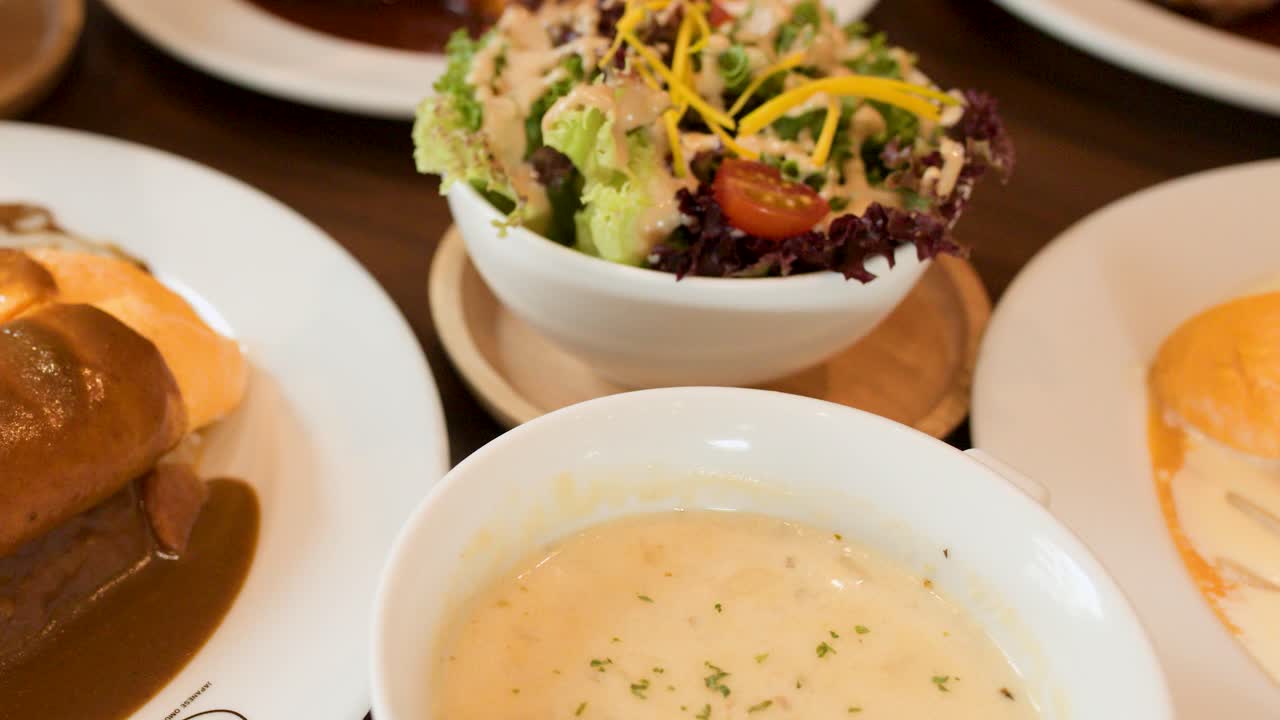 Hand slices omelette rice with brown sauce, soup, and salad in bright restaurant lighting