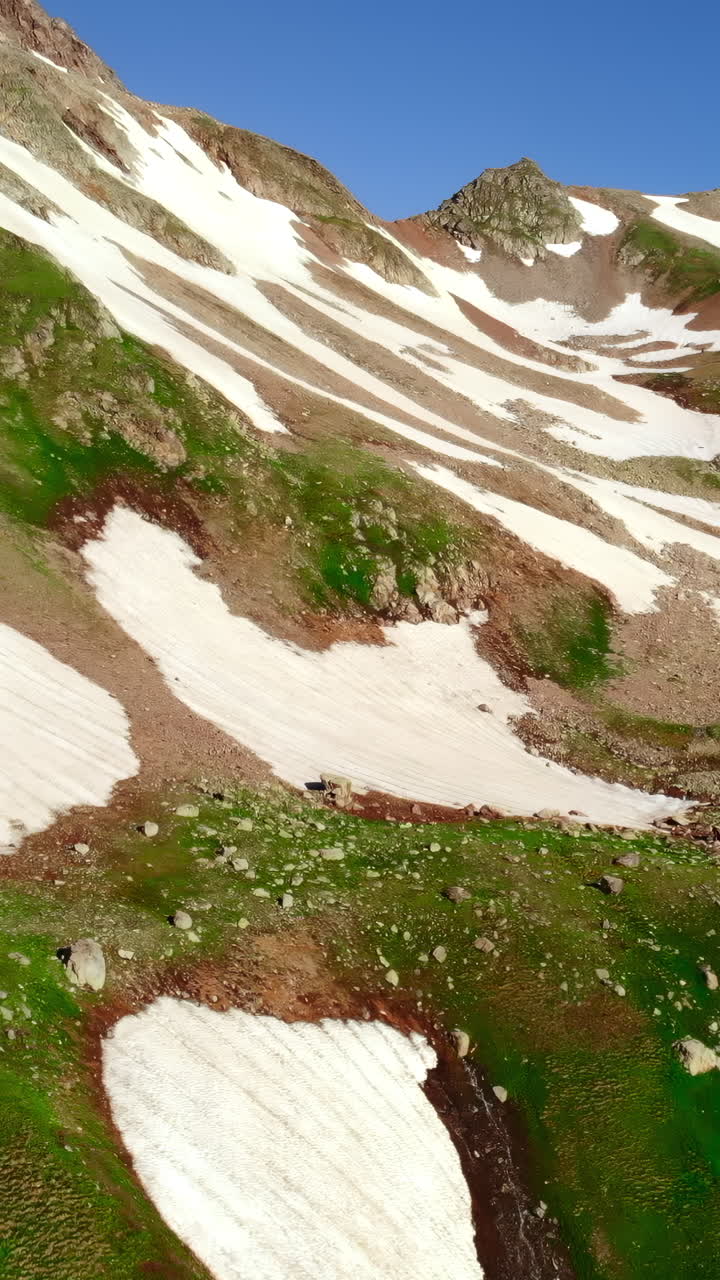 Maestoso paesaggio alpino con neve, erba verde e ruscello