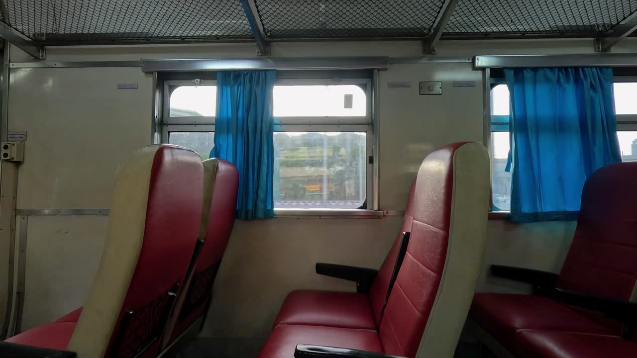 Red vinyl seats and blue curtains inside a moving train carriage, illuminated by warm sunset light, with camera panning gently past the window