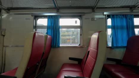 red vinyl seats and blue curtains inside a moving train carriage, illuminated by warm sunset light, with camera panning gently past the window