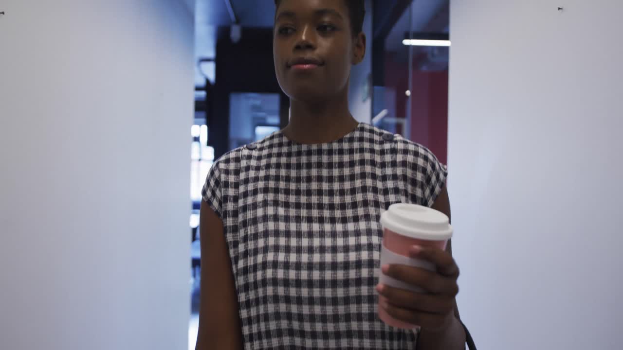 mujer de negocios afroamericana con una taza de café caminando por el corredor de la oficina