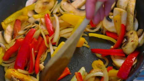 chef turning cooking vegetables including mushrooms, peppers, onions in hot frying pan in slow motion using wooden spoon 4k