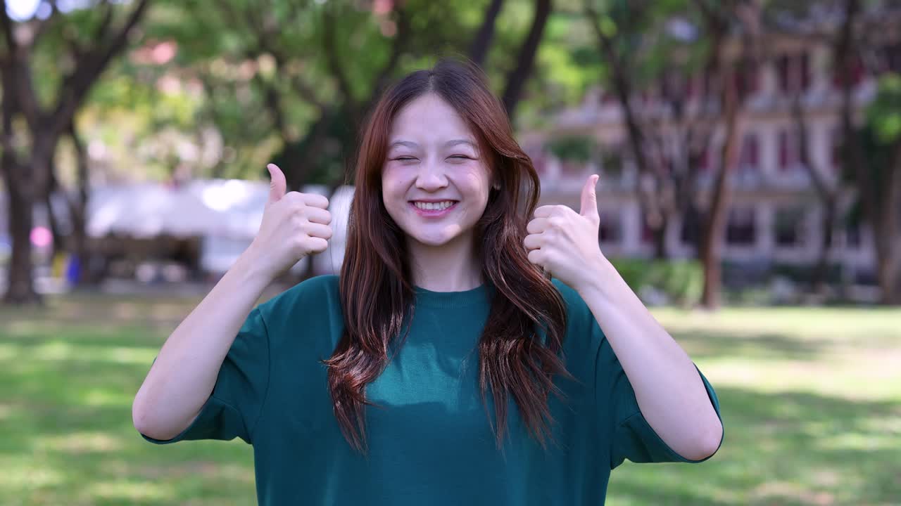公園で親指を立てている幸せそうな若いアジア人女性