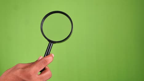 hand holding magnifying glass on green screen