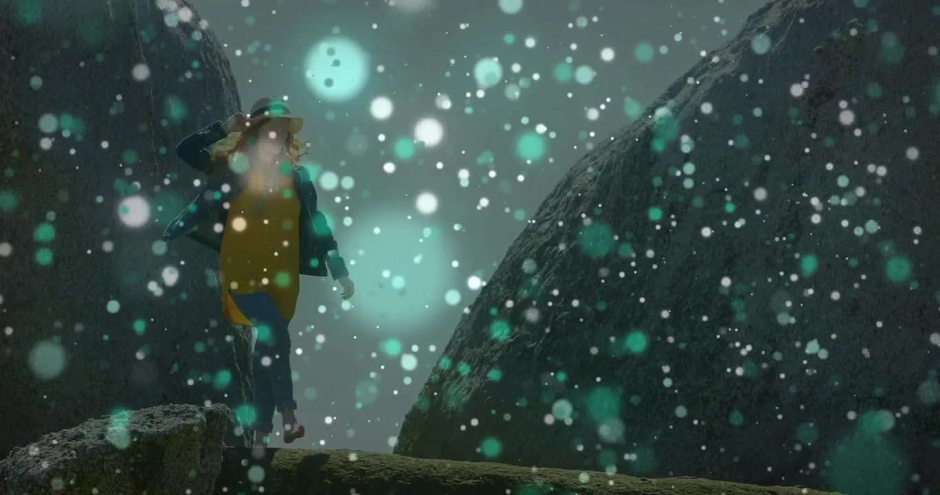 Blogger di viaggi che inizia ad attraversare una sporgenza tra massi con neve che cade, regolando il cappello per l'equilibrio