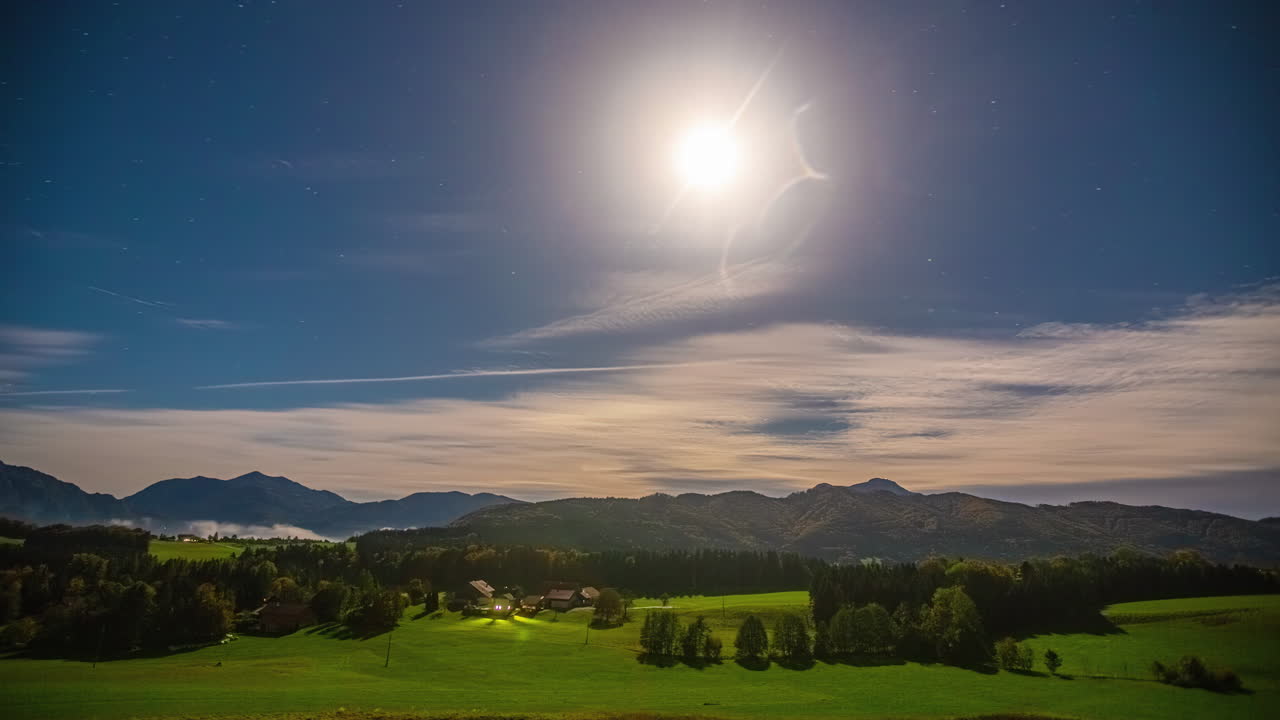 구름이 마을을  ⁇ 고 황혼으로 바뀌면서 산을 배경으로 한 달빛의 알파인 들판