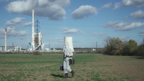 scientist in protective suit and suitcase walking field outdoors, power station or industrial background, ecological disaster concept