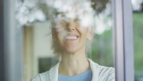 Mujer-De-Raza-Mixta-Senior-Mirando-Por-La-Ventana-Y-Sonriendo