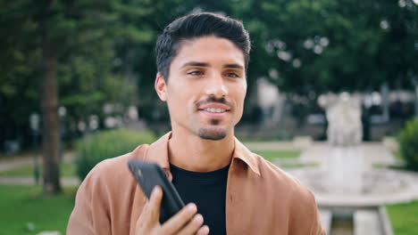 Calling-man-waving-hand-park-close-up.-Happy-guy-talking-mobile-greeting-alone