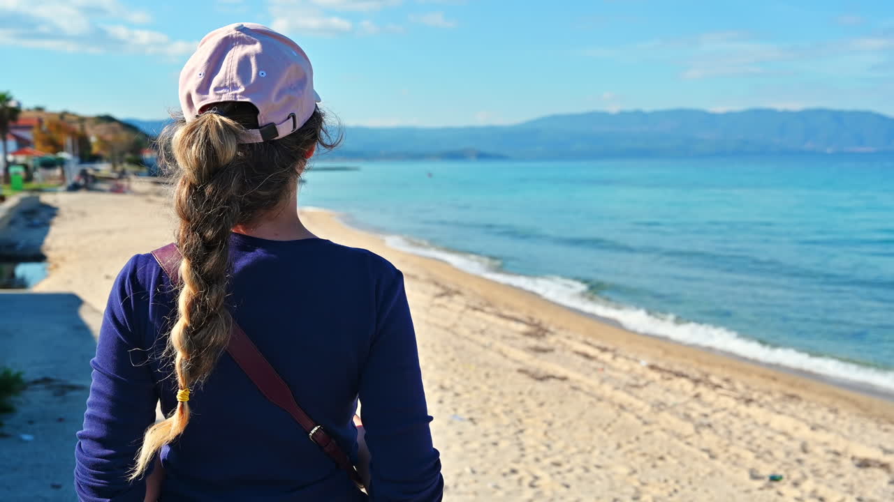 Woman watching the sea waves and mountains at the beach. Wearing pink cap and shirt