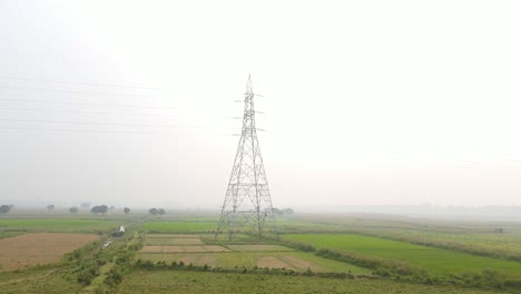 Fast-forward-moving-aerial-view-towards-electricity-power-pylon-tower-on-misty-Bangladesh-countryside-farmland-at-sunrise