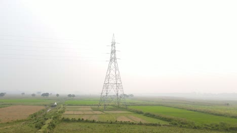 vista aérea de avance rápido hacia la torre del pilón de energía eléctrica en las tierras de cultivo del campo brumoso de bangladesh al amanecer