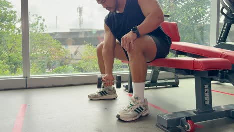 a person performs bicep curls on a bench in a well-lit gym with large windows