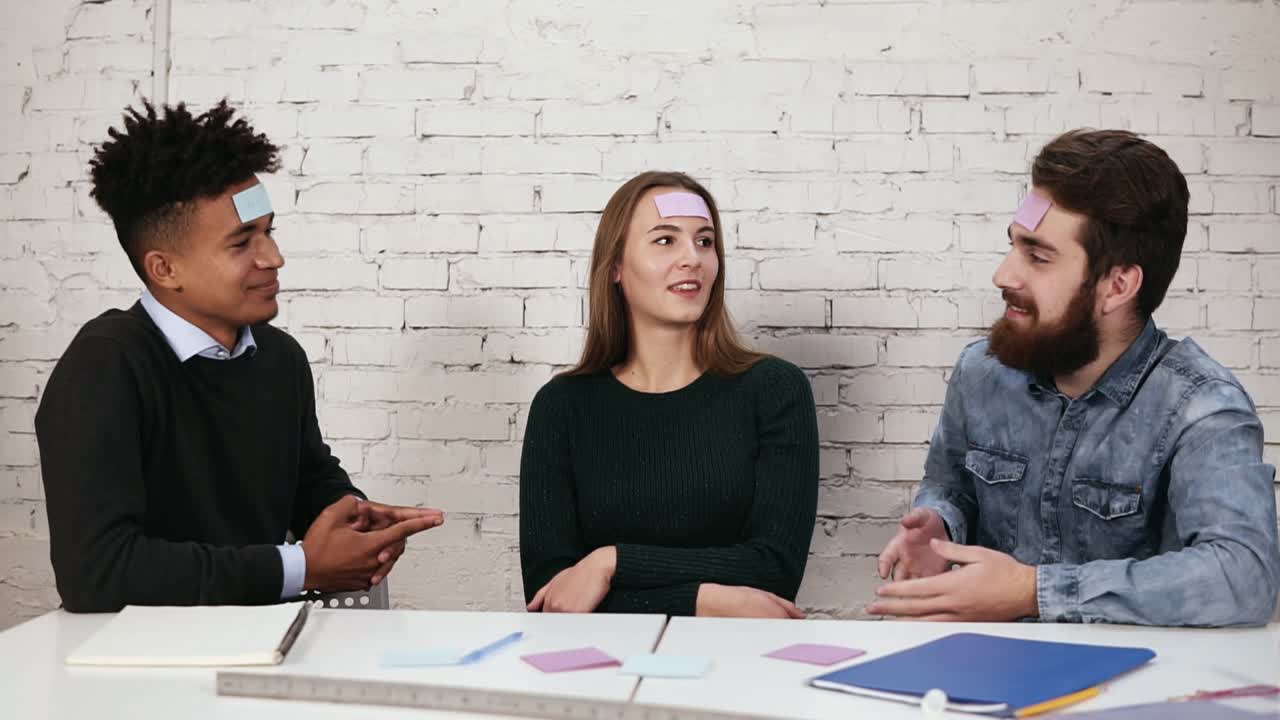 la compañía de amigos divirtiéndose en la oficina. los jóvenes pegaron pedazos de papel en la frente y adivinar palabras. diversas