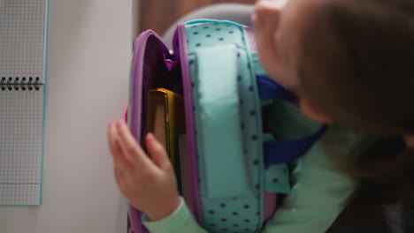 schoolgirl takes textbook out of schoolbag sitting at desk