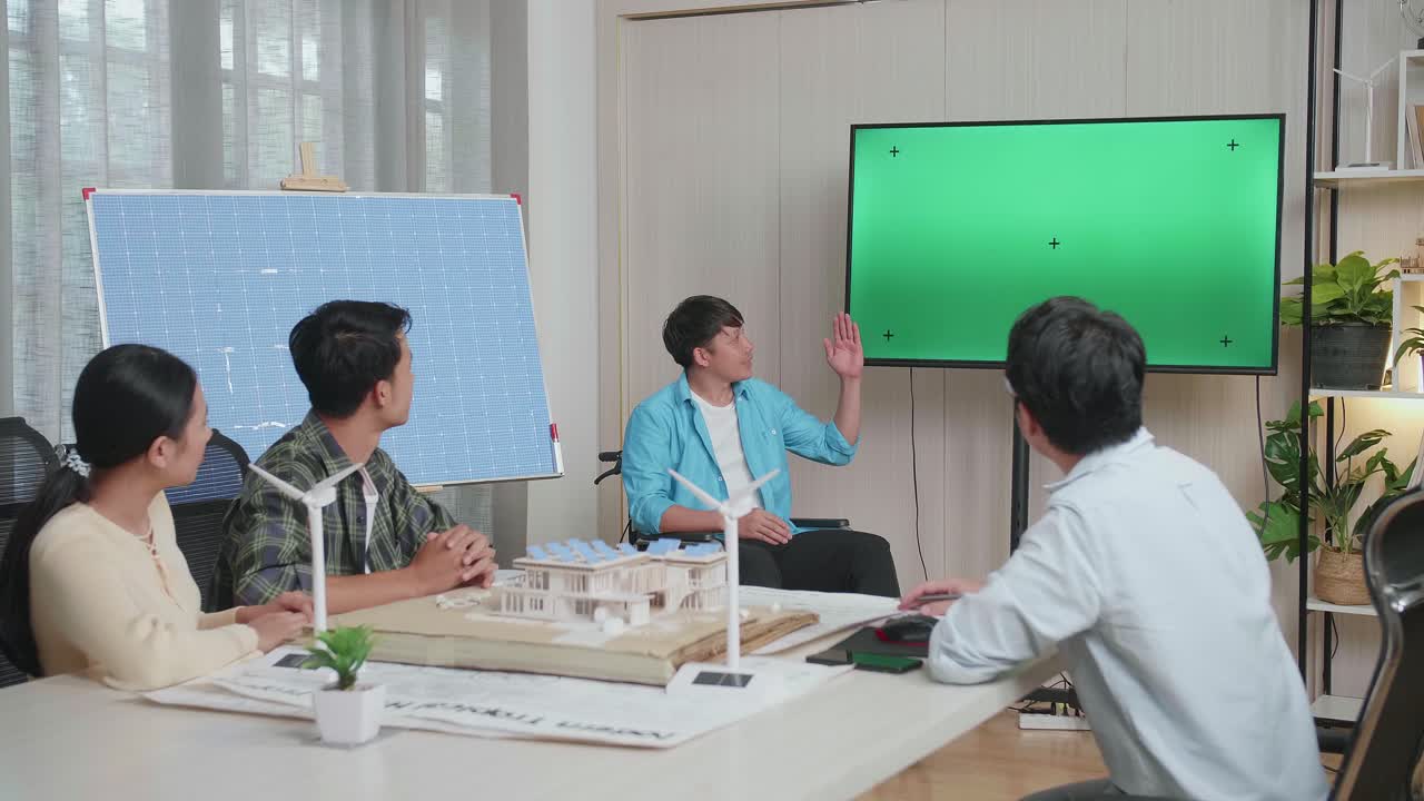 태양전지로 체어에 앉은 아시아인 엔지니어가 사무실에서 녹색 스크린 tv에 대해 발표합니다.