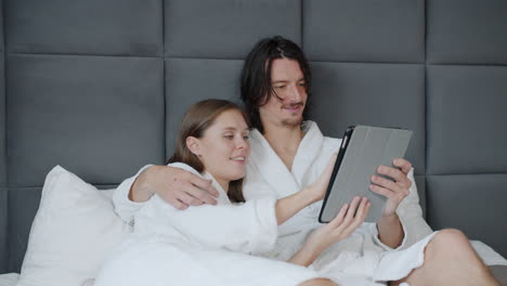 couple relaxing in bed and using tablet