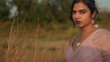 Young-woman-with-nose-ring-and-pink-earrings-in-a-field-at-sunset,-close-up