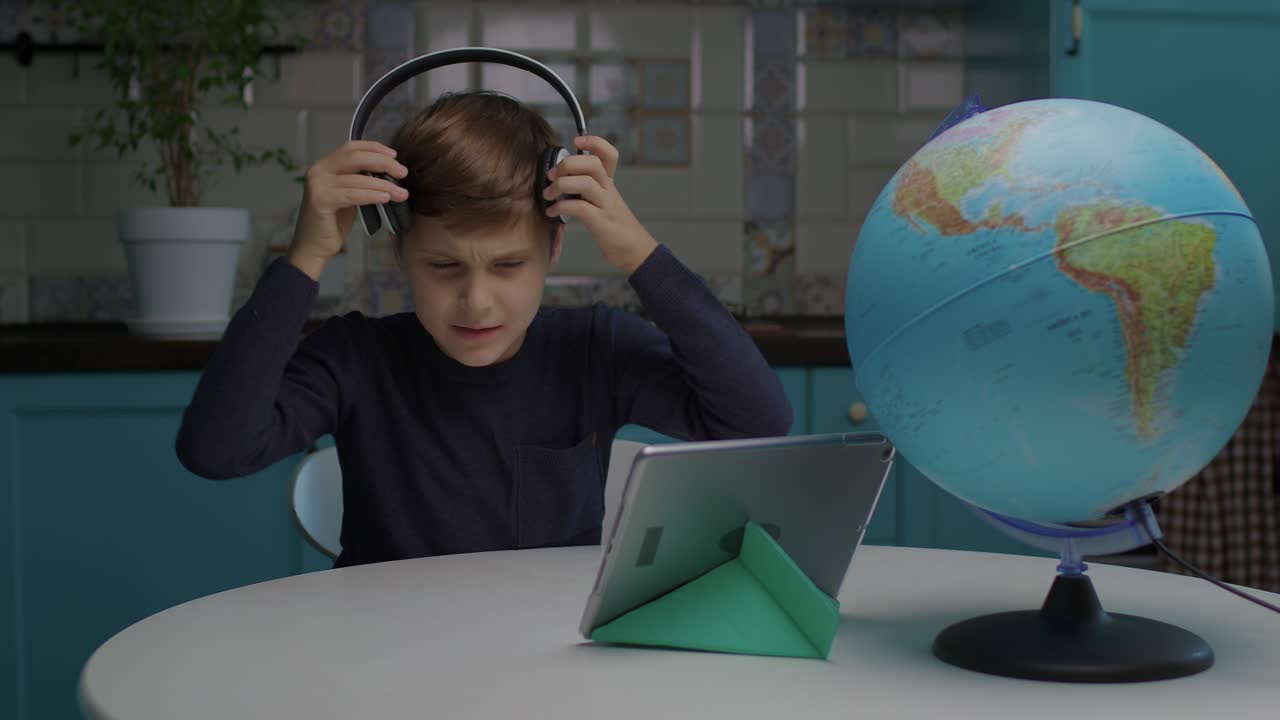 10 years old boy with autism learning online using tablet computer at home. Smiling autistic school kid studying from home.