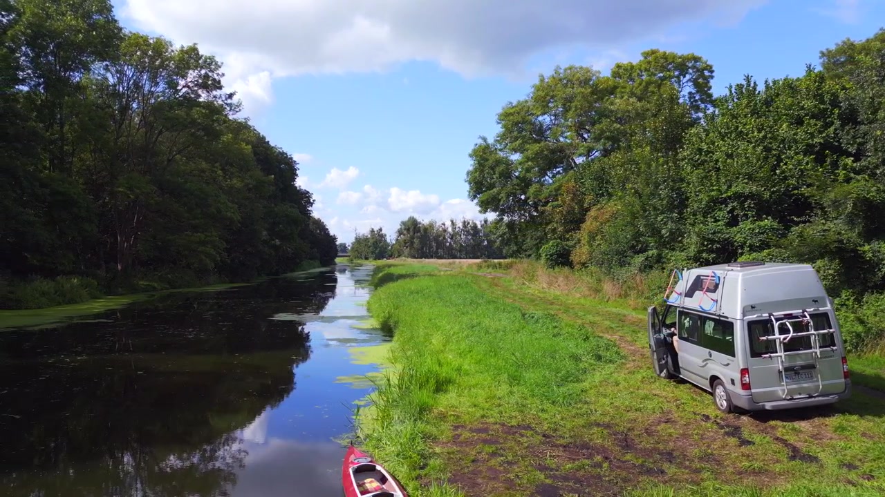 Mand ved rød pagajbåd ved bredden. Fantastisk luftfoto fra oven af autocamper ved floden, sommer 2023 i Havelland, Tyskland. 4k filmisk.