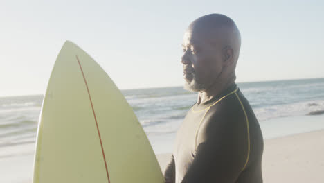 happy senior african american man holding surfboard at beach, in slow motion