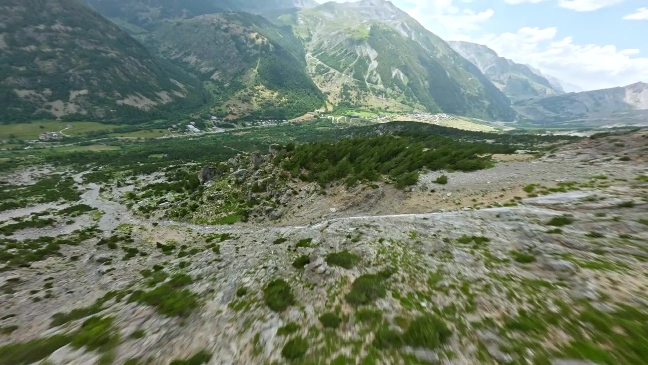Drone FPV ad alta velocità sfreccia giù per un ripido pendio montano italiano verso una valle verde sottostante.