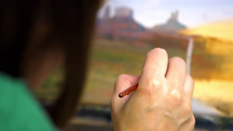 delicate artist oil painting a scenic desert scape, hand and brush in focus