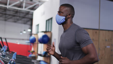 hombre afroamericano en forma con máscara facial corriendo en una cinta de correr en el gimnasio