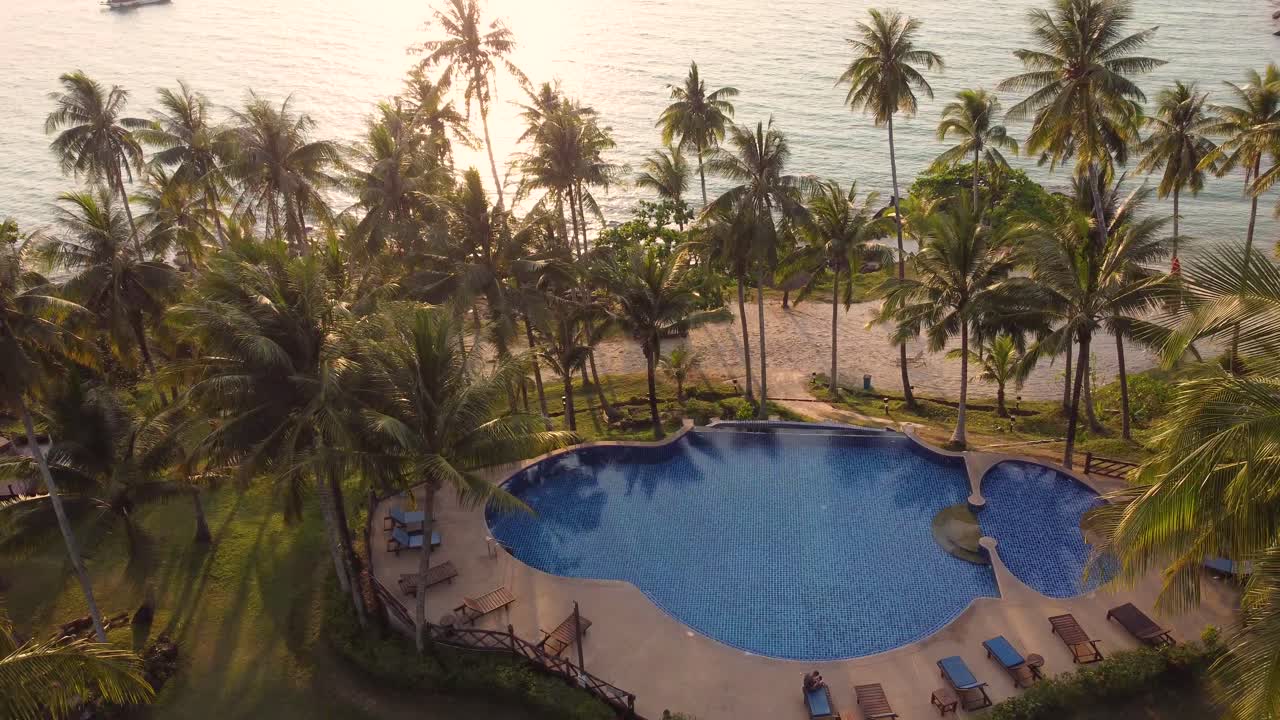 un dron tropical de 4k, volando entre palmeras con vistas a un encantador resort de playa y, al océano y a la piscina, al atardecer en la isla de koh kood en tailandia en el mar asiático