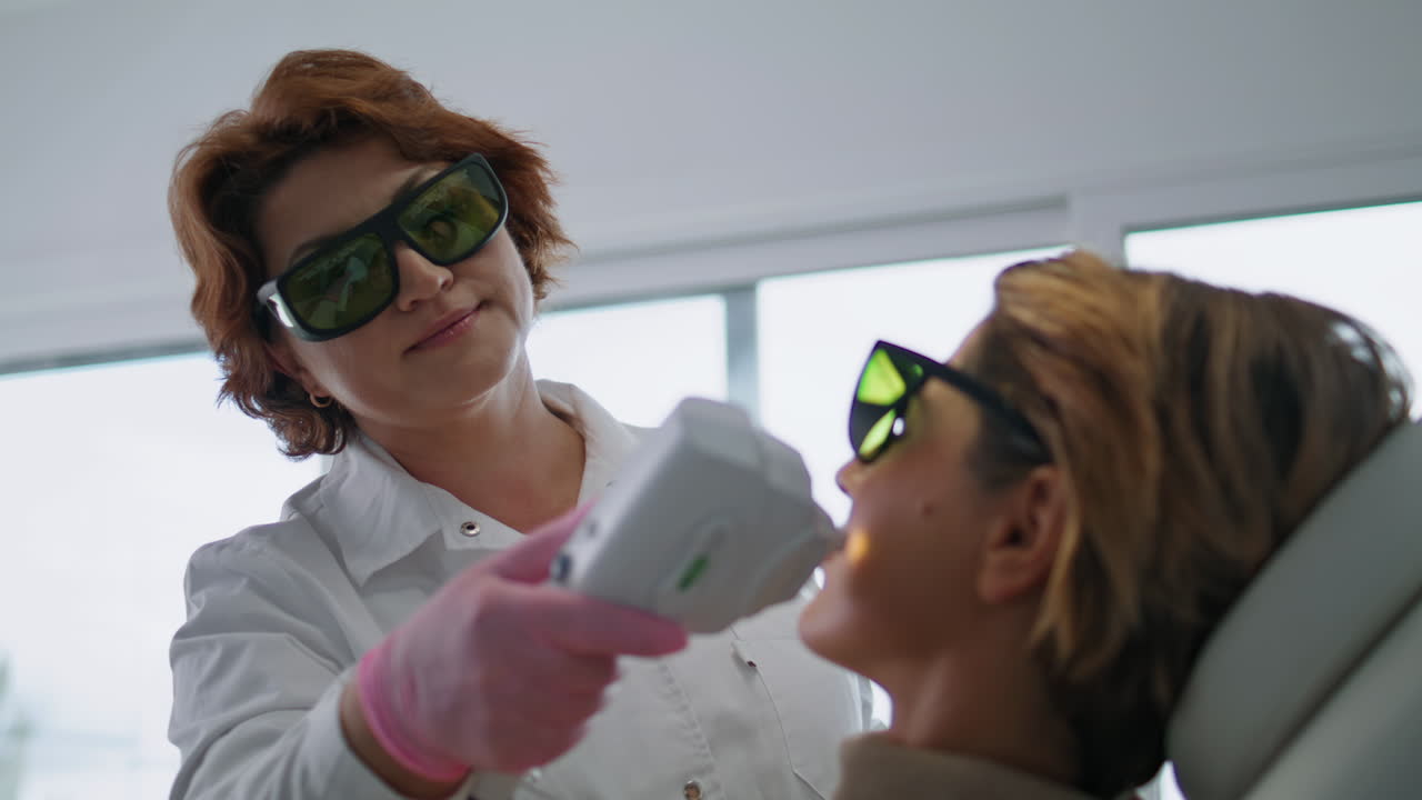 Nahaufnahme einer kosmetischen Dermatologin, die ein Lasergerät zur Hautstraffung bei einer Kundin einsetzt.