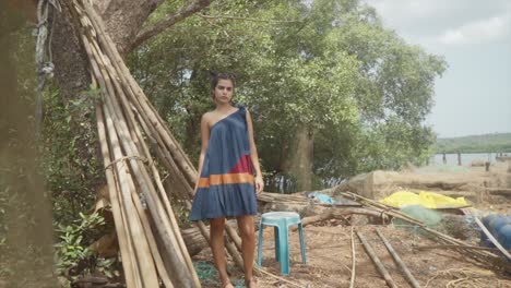 Slow-motion-shot-coming-around-the-corner-seeing-a-woman-in-a-dark-blue-dress-standing-next-to-a-pile-of-wood