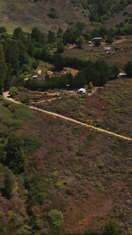 wavy road through the rocky landscape leading to the houses among the green fir-trees. mountains at backdrop. top view. vertical video