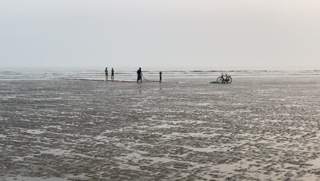 Silhouettenaufnahme-Eines-Leeren-Strandes-Mit-Einem-Fischer,-Der-Mit-Seinem-Kind-An-Seinem-Netz-Arbeitet,-Und-Einigen-Leuten,-Die-Sich-Unterhalten,-Ein-Fahrrad,-Das-In-Kalkutta-Beiseite-Geparkt-Ist