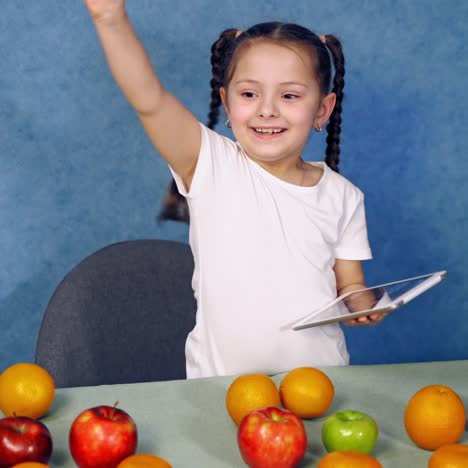 . girl using tablet at table. portrait of little girl using tablet at table with fruits